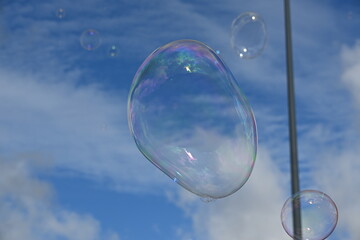 Soap bubble against a blue sky with few clouds and trees
