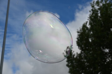 Soap bubble against a blue sky with few clouds and trees
