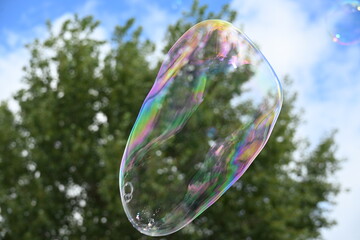 Soap bubble against a blue sky with few clouds and trees
