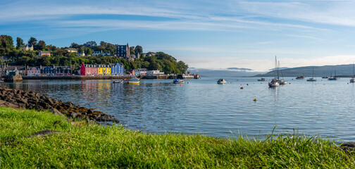 Fototapeta premium Tobermory, Schottland – bunte Häuser am Hafen bei Sonnenschein am 25. August, mit Segelbooten, Meerblick und dem Gefühl von Freiheit 