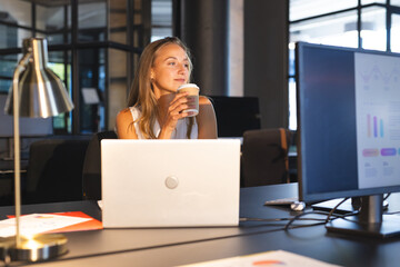Businesswoman enjoying coffee while working late at office with laptop