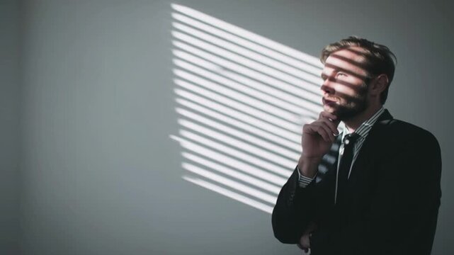 Pensive business man  in formal suit thinking and analyzing ideas in office with window blinds shadow, concept of decision making planning leadership creativity brainstorming reflection corporate mind
