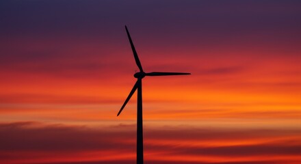Obraz premium Wind turbine silhouetted against vibrant sunset sky 