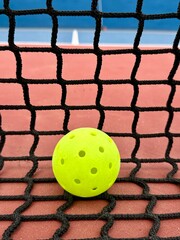 Pickleball ball close up on the hard surface by the net. Yellow perforated, hollow plastic ball for pickleball sport