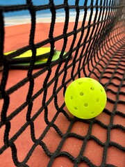 Pickleball ball close up on the hard surface by the net. Yellow perforated, hollow plastic ball for pickleball sport