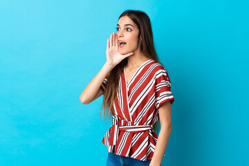 Young caucasian woman isolated on blue background shouting with mouth wide open to the side