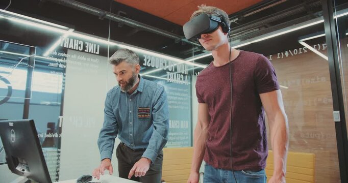 NEW YORK - April 5, 2017:Two attractive men testing virtual reality glasses. Man typing on computer keyboard. Research Centre. Young man looking around, using new invention.