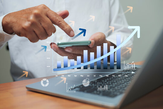 Businessman using smartphone and laptop with growth chart and rising bar graph, concept of business success, financial performance, data analytics, profit increase, and digital marketing strategy.