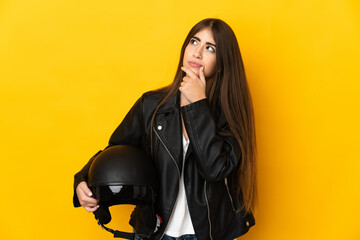 Young caucasian woman holding a motorcycle helmet isolated on yellow background having doubts