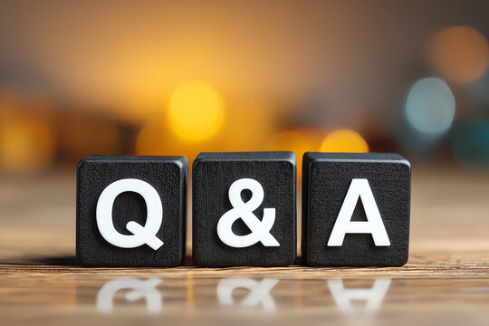 Black blocks with white letters Q, &, and A on a wooden surface, representing the concept of questions and answers with blurred warm bokeh lights in the background