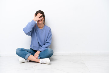 Young caucasian woman sitting on the floor isolated on white background covering eyes by hands and smiling