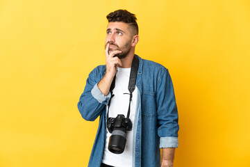 Photographer man isolated on yellow background having doubts while looking up