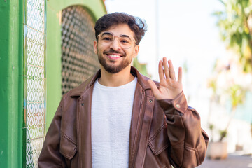 Handsome Arab man at outdoors saluting with hand with happy expression