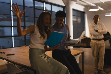 Colleagues celebrating success with laptop and documents in modern office at night