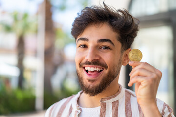 Handsome Arab man at outdoors holding a Bitcoin