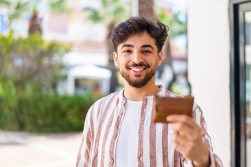 Handsome Arab man holding a wallet at outdoors with happy expression