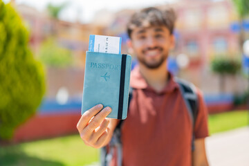 Young Arabian handsome man at outdoors holding a passport with happy expression