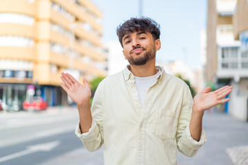 Young Arabian handsome man at outdoors making doubts gesture