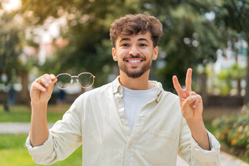 Young Arabian handsome man with glasses at outdoors smiling and showing victory sign