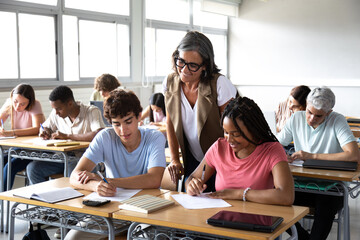Senior teacher helping diverse high school students studying in classroom