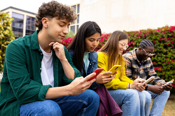 University students using smartphones sitting together outdoors