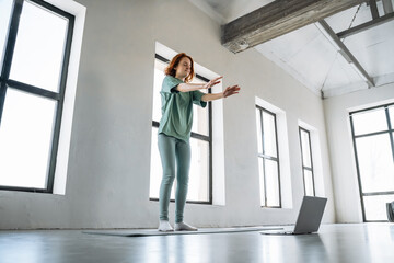 Fototapeta premium Woman practicing yoga at home using a laptop in a bright, spacious room