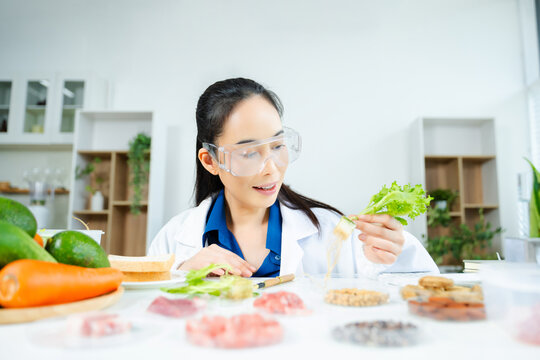 Female food scientist in lab coat and goggles analyzing fresh lettuce roots. Organic farming, hydroponics, nutrition science, and healthy research lab.