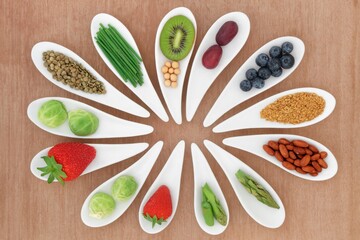 Naklejka premium Healthy food selection arranged in white ceramic spoons on wooden background, colorful assortment of fruits, vegetables, nuts, seeds and legumes in a circular pattern