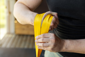 Close-up of muscular man in black shirt wrapping bright yellow strap for wrist strengthening during home armwrestling training for strong forearms. Armwrestling supination exercise with a weight.