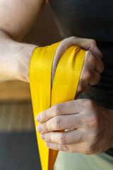 Close-up of muscular man in black shirt wrapping bright yellow strap for wrist strengthening during home armwrestling training for strong forearms. Armwrestling supination exercise with a weight.