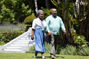 Senior couple walking hand in hand through lush garden, enjoying sunny day