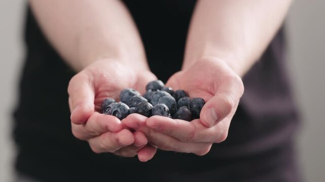 Slow motion man hands show wet washed ripe blueberries on neutral background