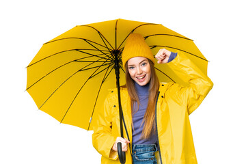 Young pretty woman with rainproof coat and umbrella over isolated chroma key background celebrating...