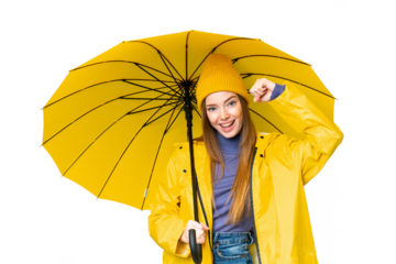 Young pretty woman with rainproof coat and umbrella over isolated chroma key background celebrating a victory