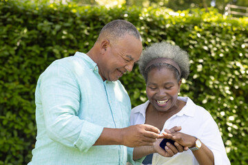 Exchanging rings and smiling, African American senior couple celebrating love in garden