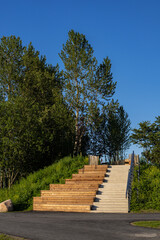 Modern wooden and concrete stairs at Putukaväil green corridor near Paavli, Tallinn, Estonia. Surrounded by lush greenery and tall trees under clear blue summer sky, urban park architecture detail.