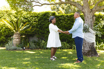 Senior couple holding hands in garden, smiling and enjoying sunny day together