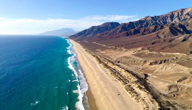 Wide sandy beach borders turquoise water, reaching mountains beneath a bright sky