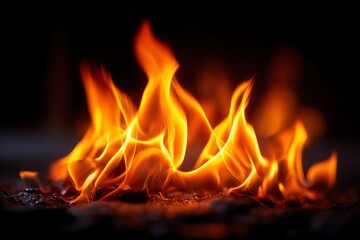 Fototapeta premium Fiery scene showcasing bright orange flames licking upwards from a dark textured base against a black backdrop
