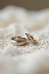 A close-up of wedding rings resting on a delicate lace fabric. Soft light highlights the intricate details of the rings and lace