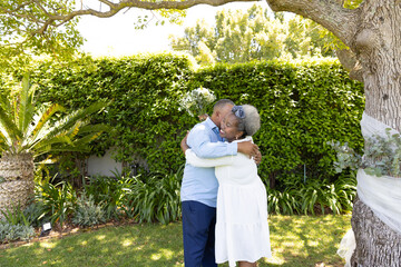Senior couple embracing under tree in garden, enjoying peaceful moment together