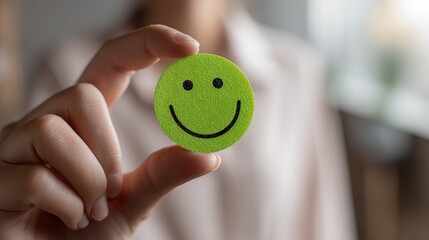 Close up photo of hand holding bright green smiley face sticker with blurred background, soft natural light and shallow depth of field, symbolizing positivity and support for World Mental Health Day