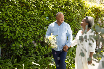 Senior couple walking in garden holding hands, enjoying sunny day together