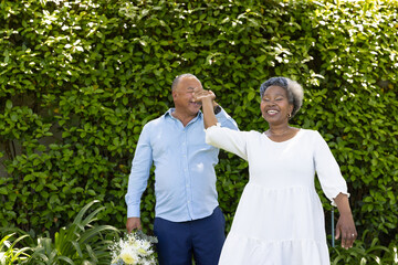 Senior couple dancing joyfully in garden, holding hands and smiling brightly