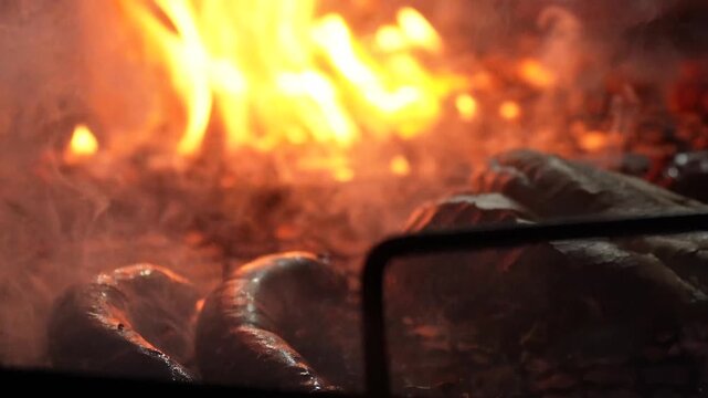 Large, spiral-shaped sausages are grilled on a smoky grill. Thick smoke from the coals creates a light smoky effect, and the warm, inviting colors of the cooked meat create a mouth-watering picture.