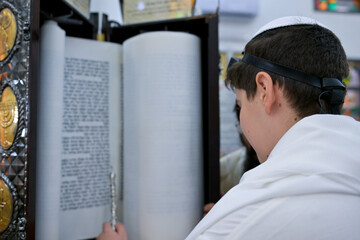 A bar mitzvah boy reading from the Torah scroll in a synagogue.