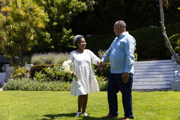 Senior couple holding hands and smiling while walking together in sunny garden