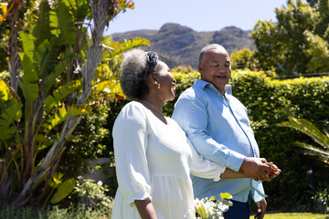 Senior couple walking in sunny garden, holding hands and smiling joyfully