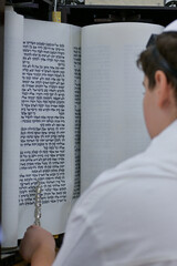 A bar mitzvah boy reading from the Torah scroll in a synagogue.