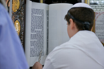 A bar mitzvah boy reading from the Torah scroll in a synagogue.